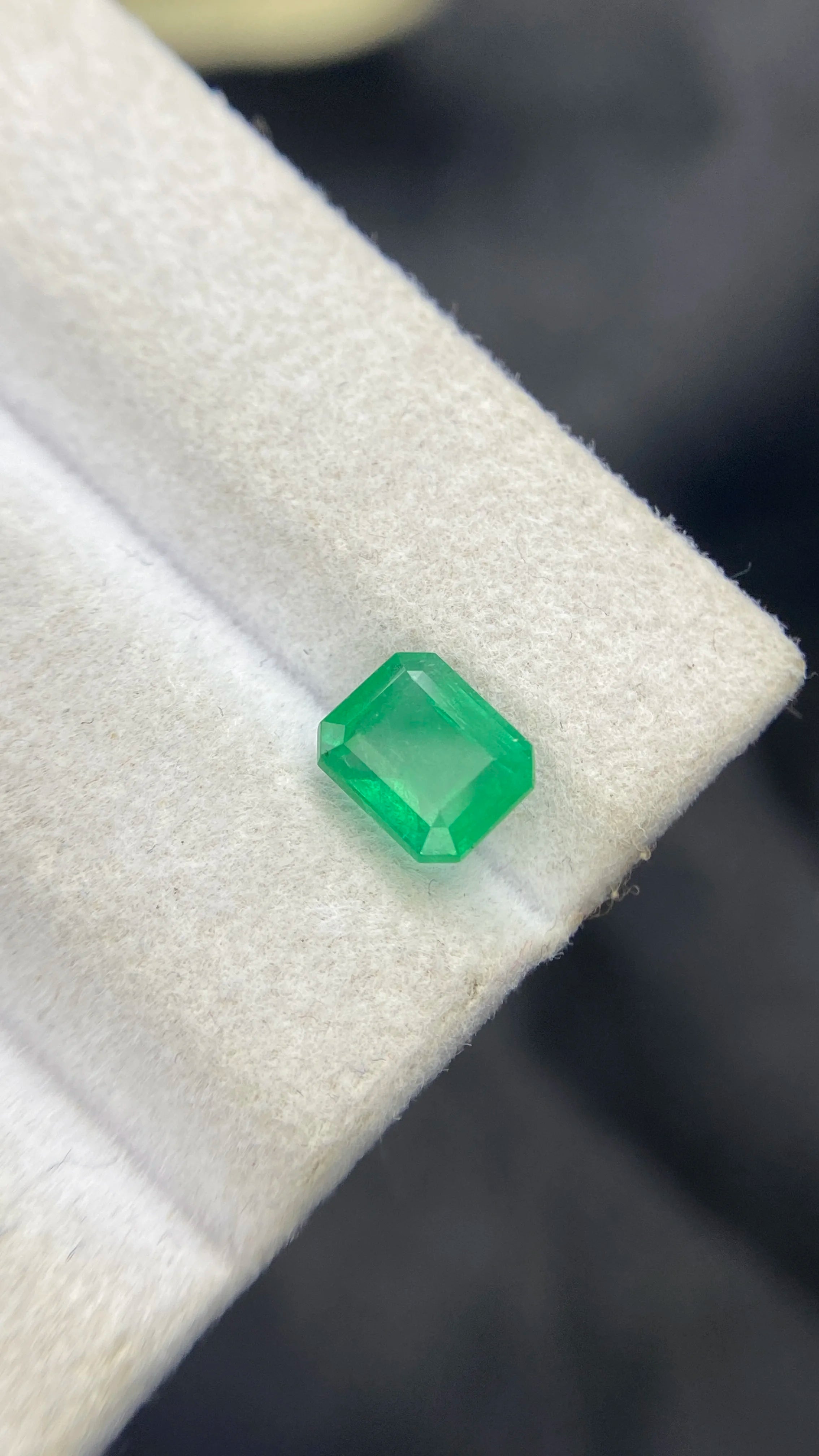Green emerald-cut gemstone on white pad, angled close-up