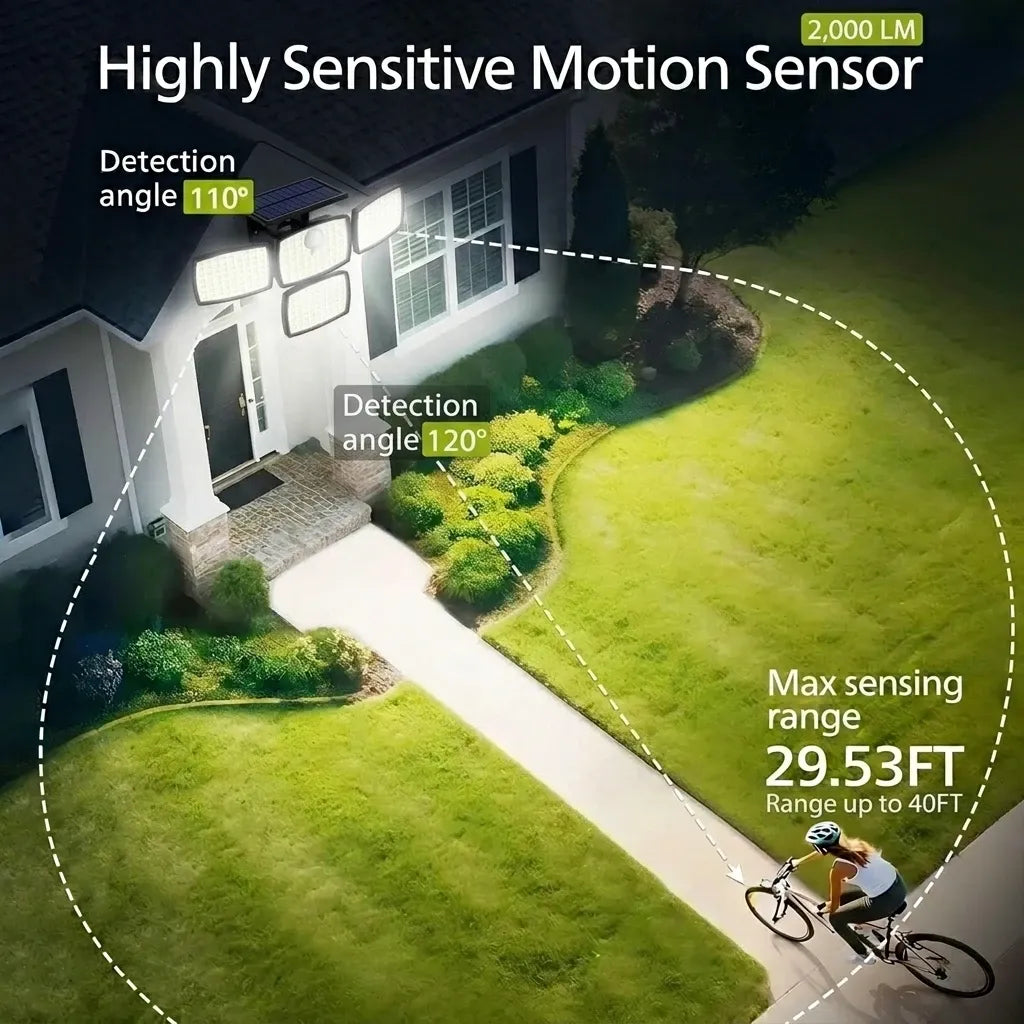 Black 4-head solar flood light mounted on a house exterior, illuminating a front yard pathway with bright light.