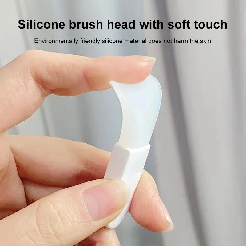 Hand holding a small, flexible white silicone facial mask applicator tool with a curved, spatula-style brush head.