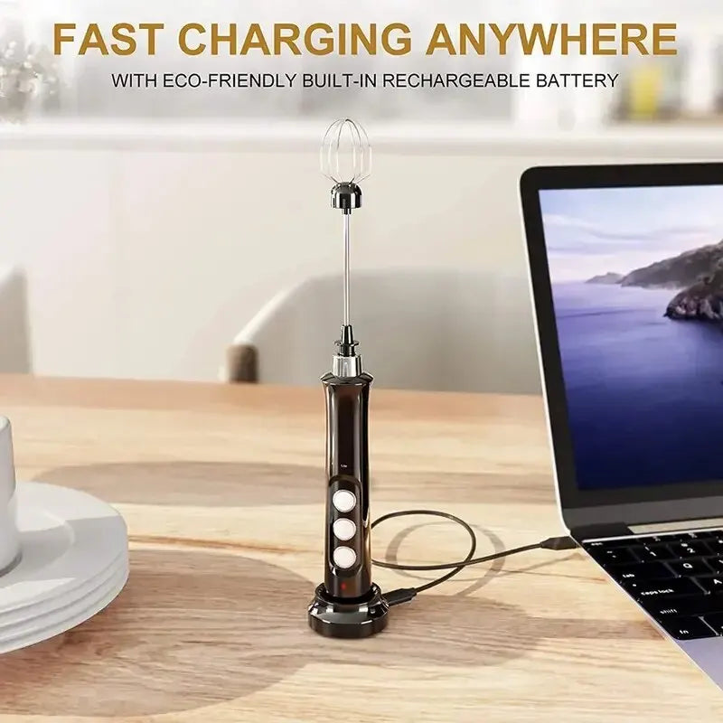 Black handheld electric milk frother with rechargeable battery and charging stand plugged into a laptop.