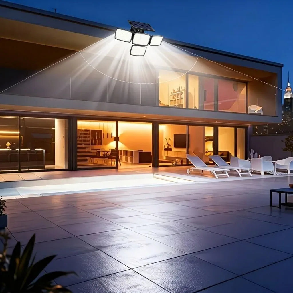Black 4-head solar flood lamp mounted on a modern home's exterior wall, casting bright light over a patio.