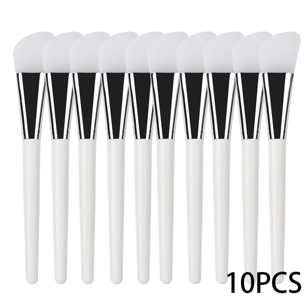 Ten silicone face mask brushes with white tips, silver ferrules, and white handles arranged in a row.