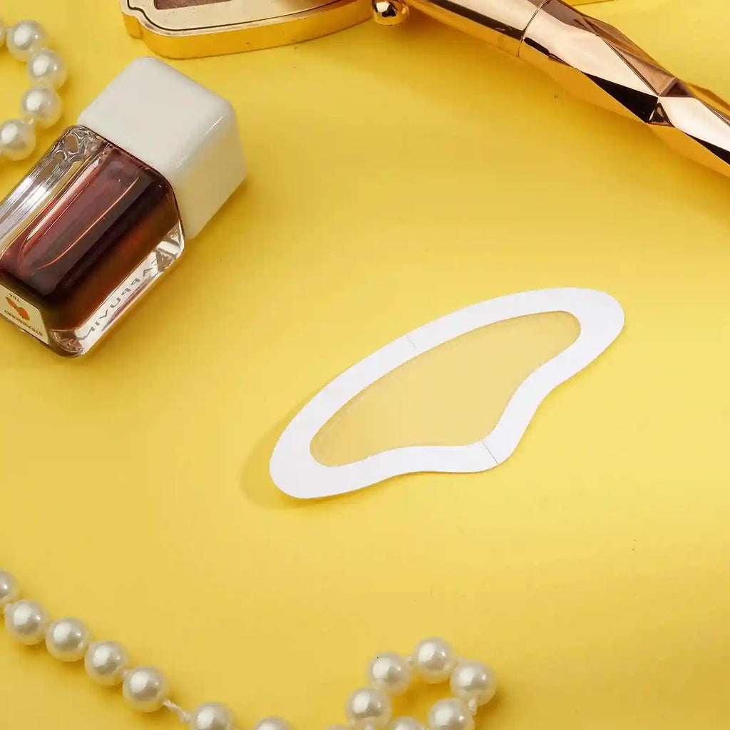A clear, wing-shaped microneedle forehead patch on a yellow background with beauty accessories.