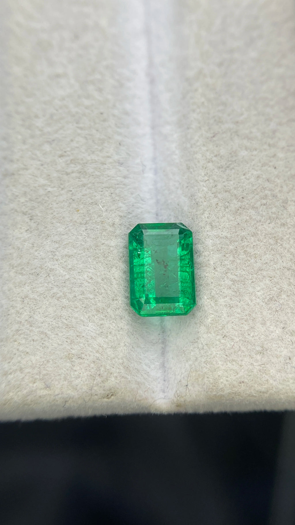 Green emerald-cut rectangular gemstone, loose faceted stone centered on white padding