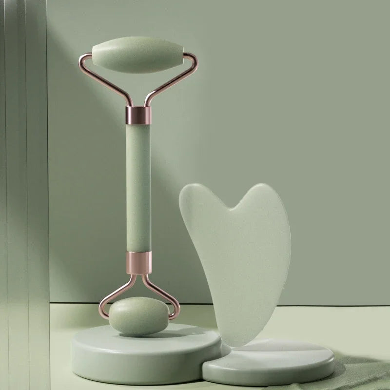 A mint green face roller with rose gold accents and a matching heart-shaped gua sha tool on a cylindrical pedestal.