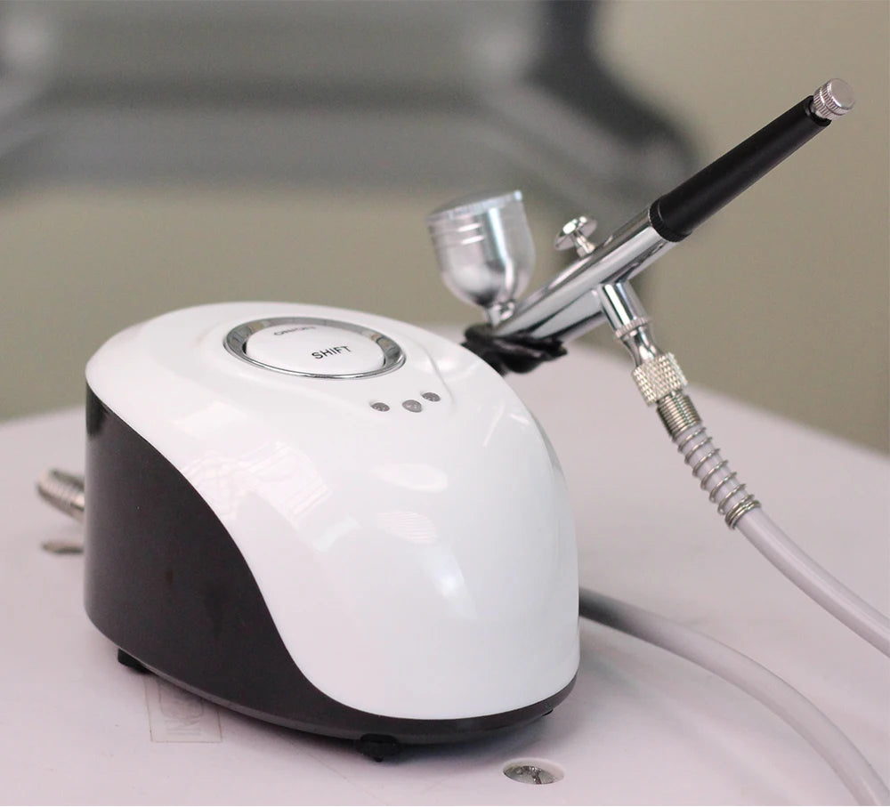 Portable white and black airbrush compressor machine with a metallic airbrush gun connected by a hose.