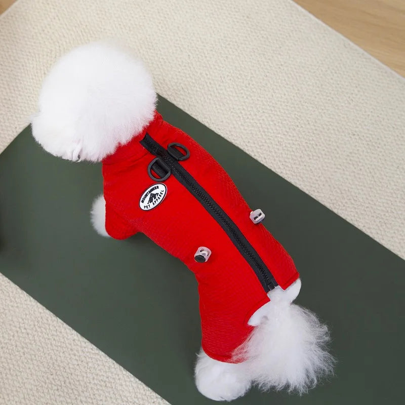 Small white dog wearing a red waterproof winter jumpsuit with a harness leash attachment for warm outdoor walks.