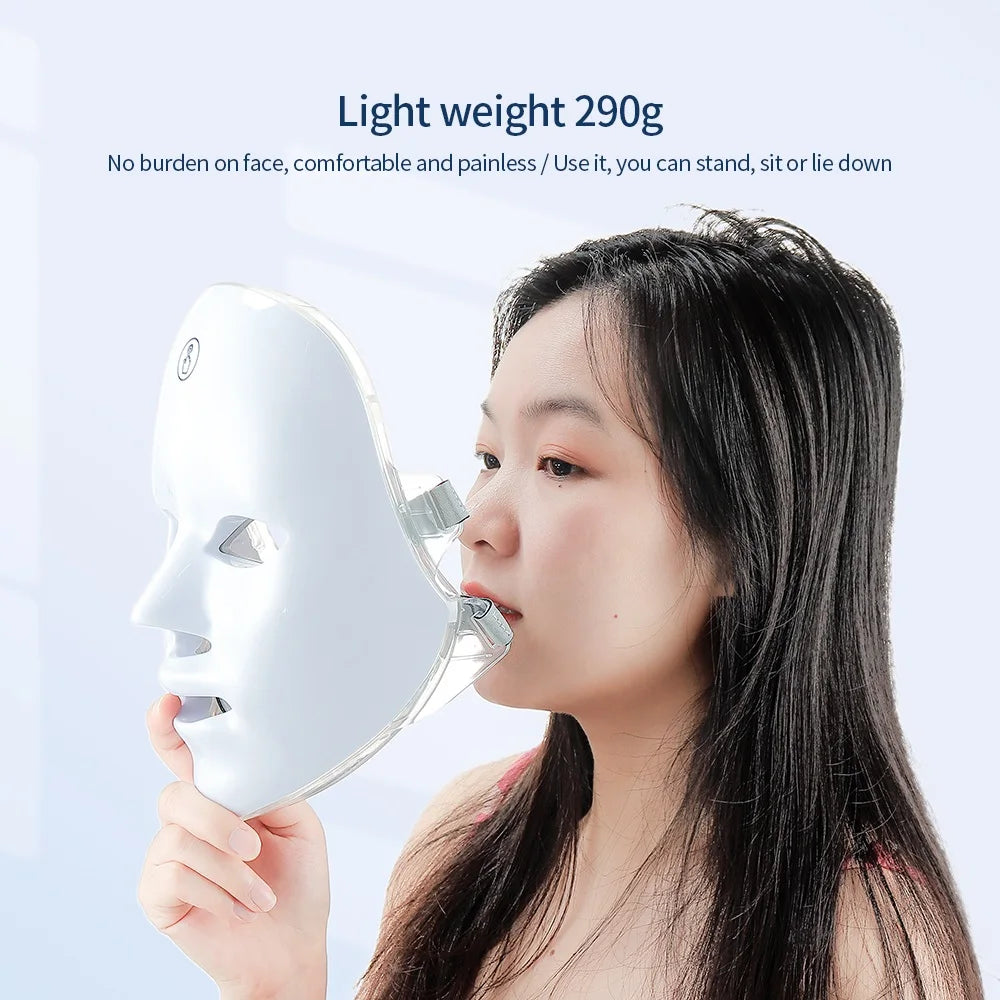 A woman holding a sleek, white, ergonomic LED face mask for skincare rejuvenation against a light blue background.