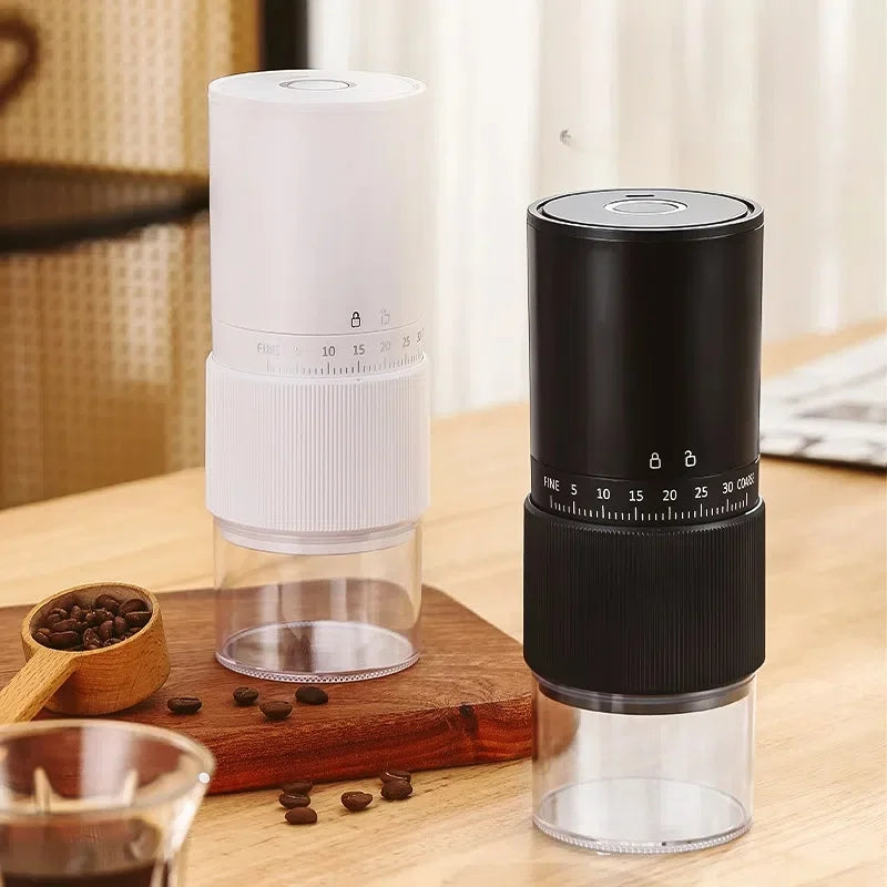 Black and white portable coffee grinders with adjustable grind settings and clear grounds canisters on a wooden board.