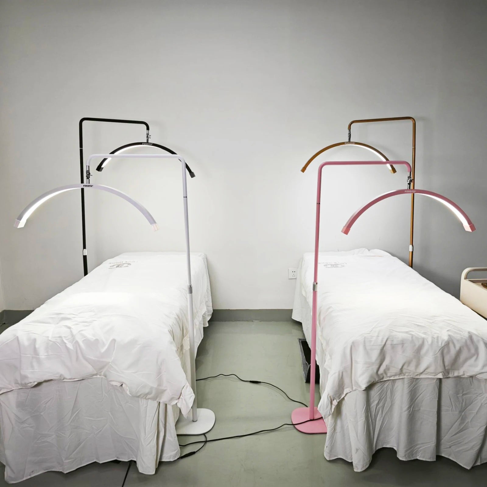 Crescent-shaped LED floor lamps with metal stands over spa beds, available in black, white, pink, and gold finishes.