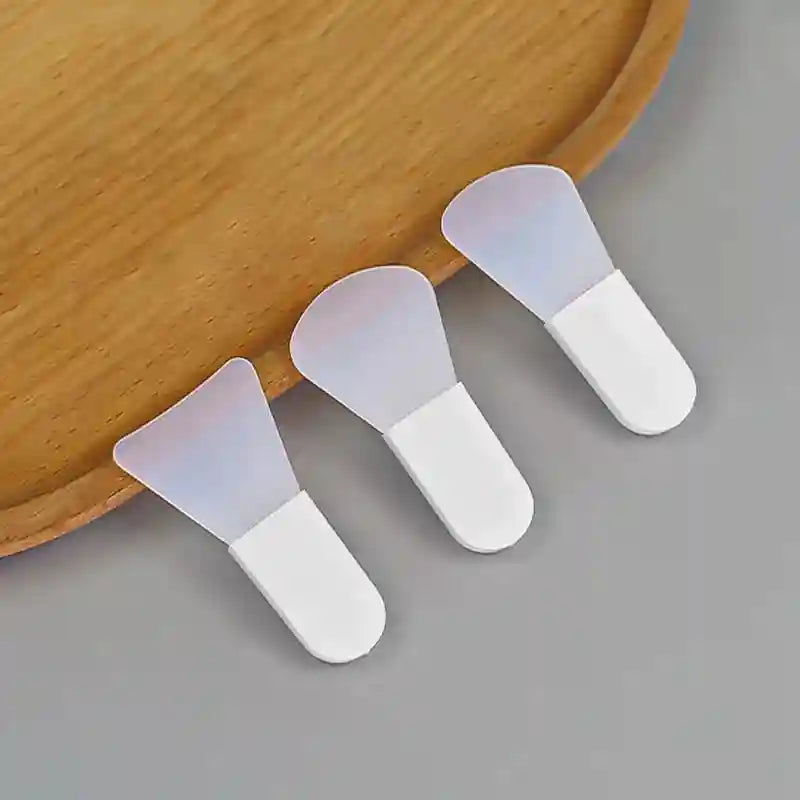 Three silicone facial mask applicators with opaque white handles and translucent, flexible spatula heads.