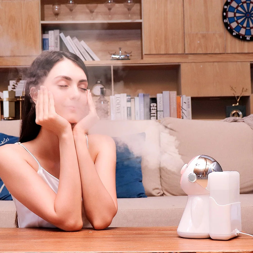 White astronaut-shaped desktop facial steamer emitting a cool mist toward a woman sitting at a wooden table.